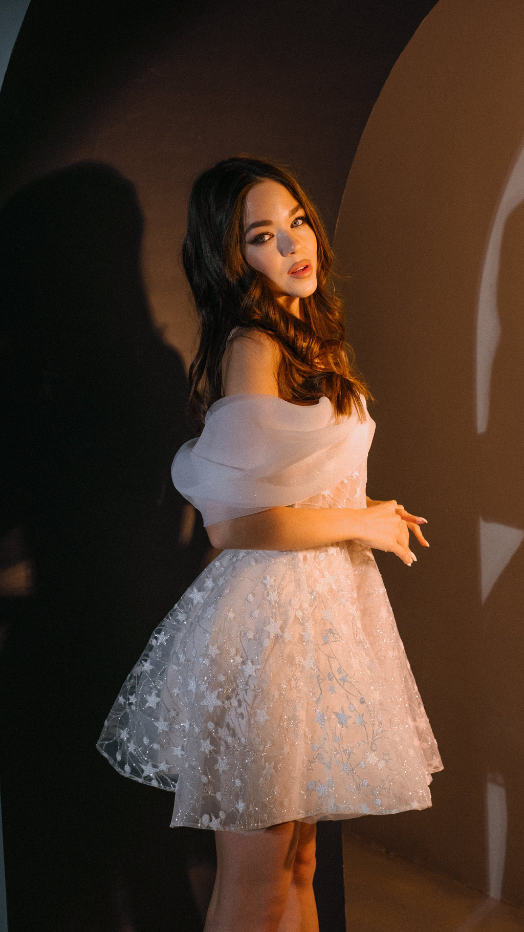 Model glancing over her shoulder in an off-shoulder star mini wedding dress, dark studio backdrop, Shooting Star