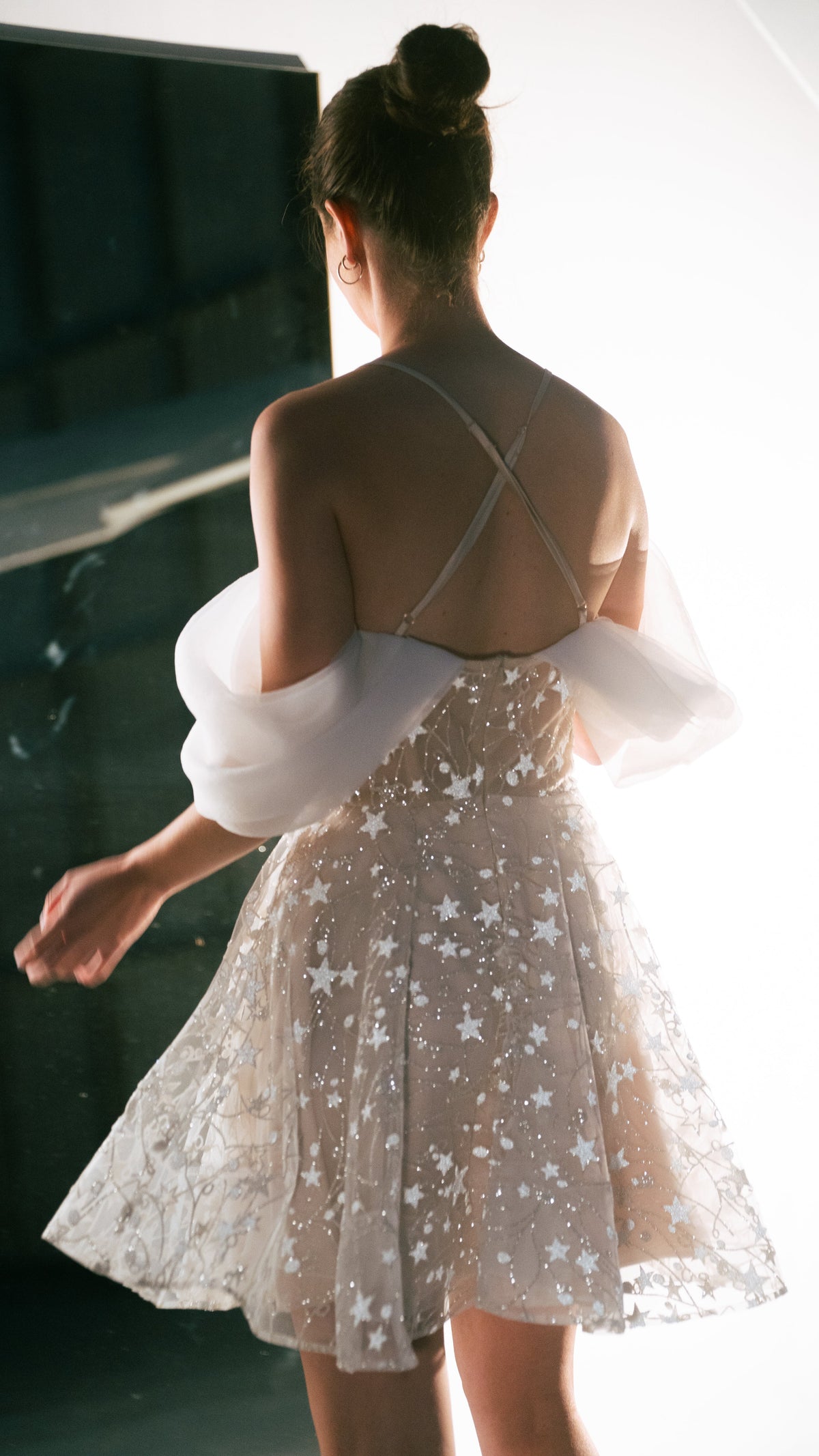 Back view of a star lace mini wedding dress with crossed straps and off-shoulder drapes, bright studio, Shooting Star