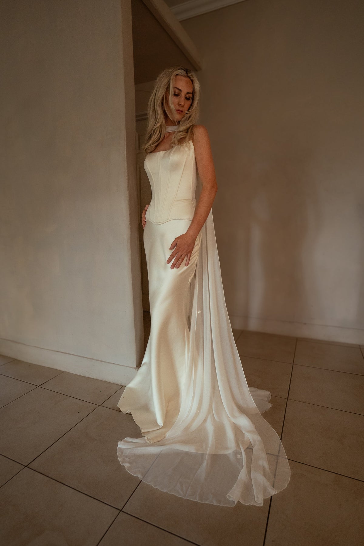 Satin bridal corset and fitted skirt with a fanned train on a tiled floor, bride resting her hand on her hip, Solana Corset