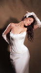 Satin corset and skirt bridal separates, bride with a gloved hand resting on her head, warm dark backdrop, Solana Ensemble