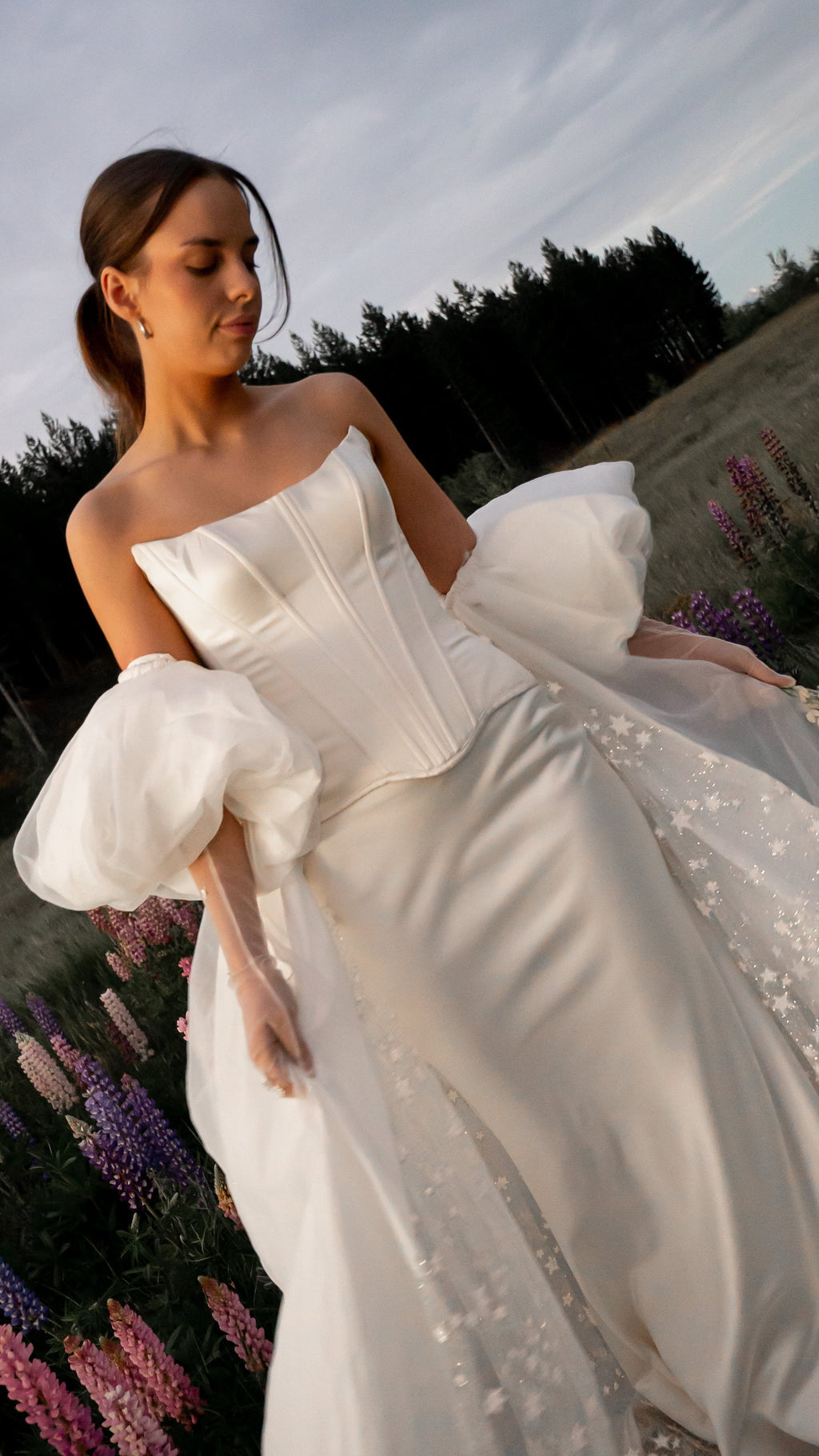 Bride walking through a wildflower field in satin bridal separates with organza puff sleeves and a star train, Solana Ensemble