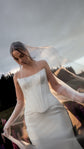 Satin corset and skirt bridal separates seen through a sheer veil drawn over the bride's head, cloudy evening sky, Solana Ensemble