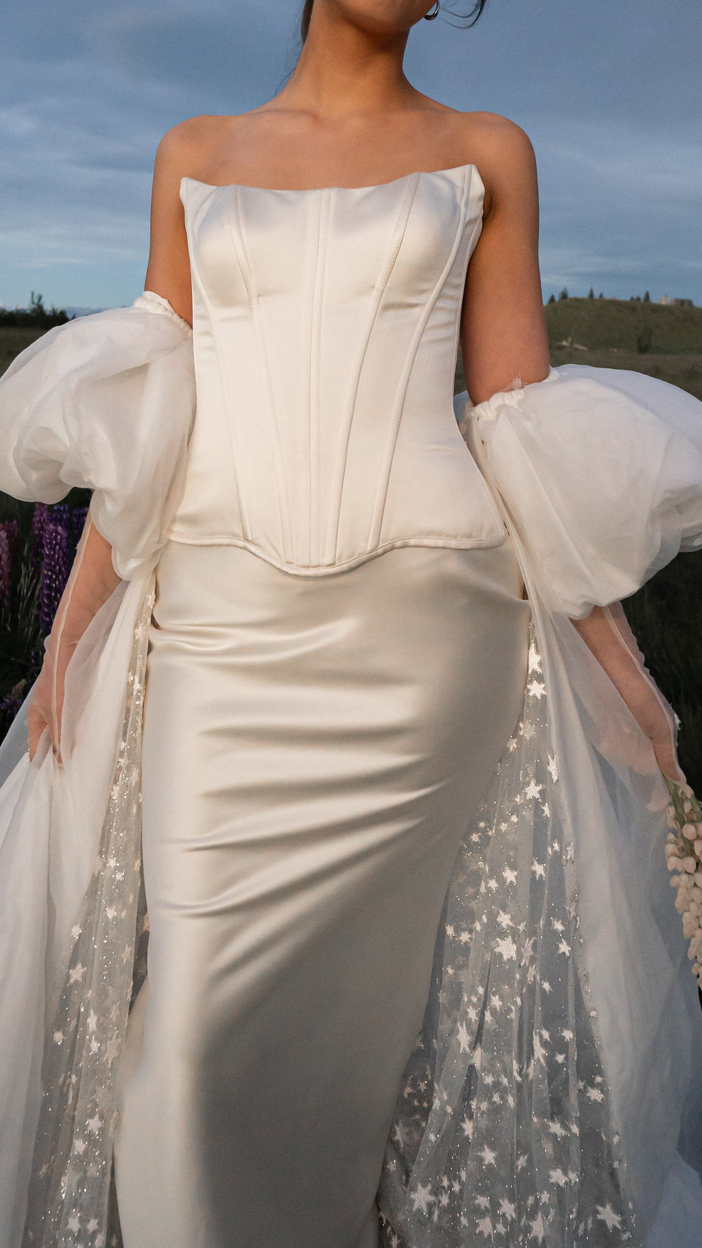 Torso crop of a satin bridal skirt with a dropped waist under a boned corset, organza puff sleeves, evening field, Solana Skirt