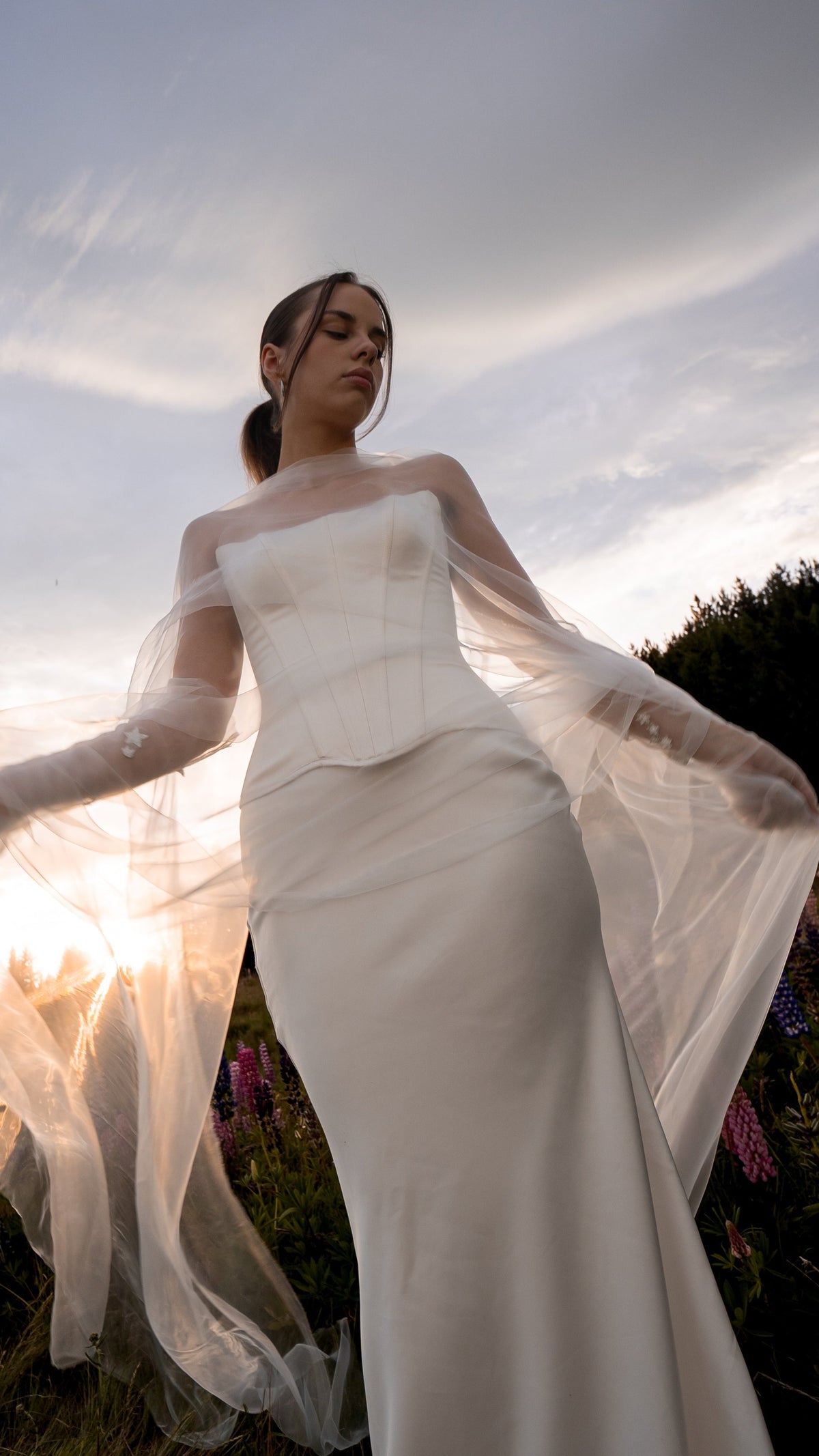 Low-angle shot of a satin bridal skirt and corset with a sheer tulle wrap billowing at sunset, ethereal, Solana Skirt