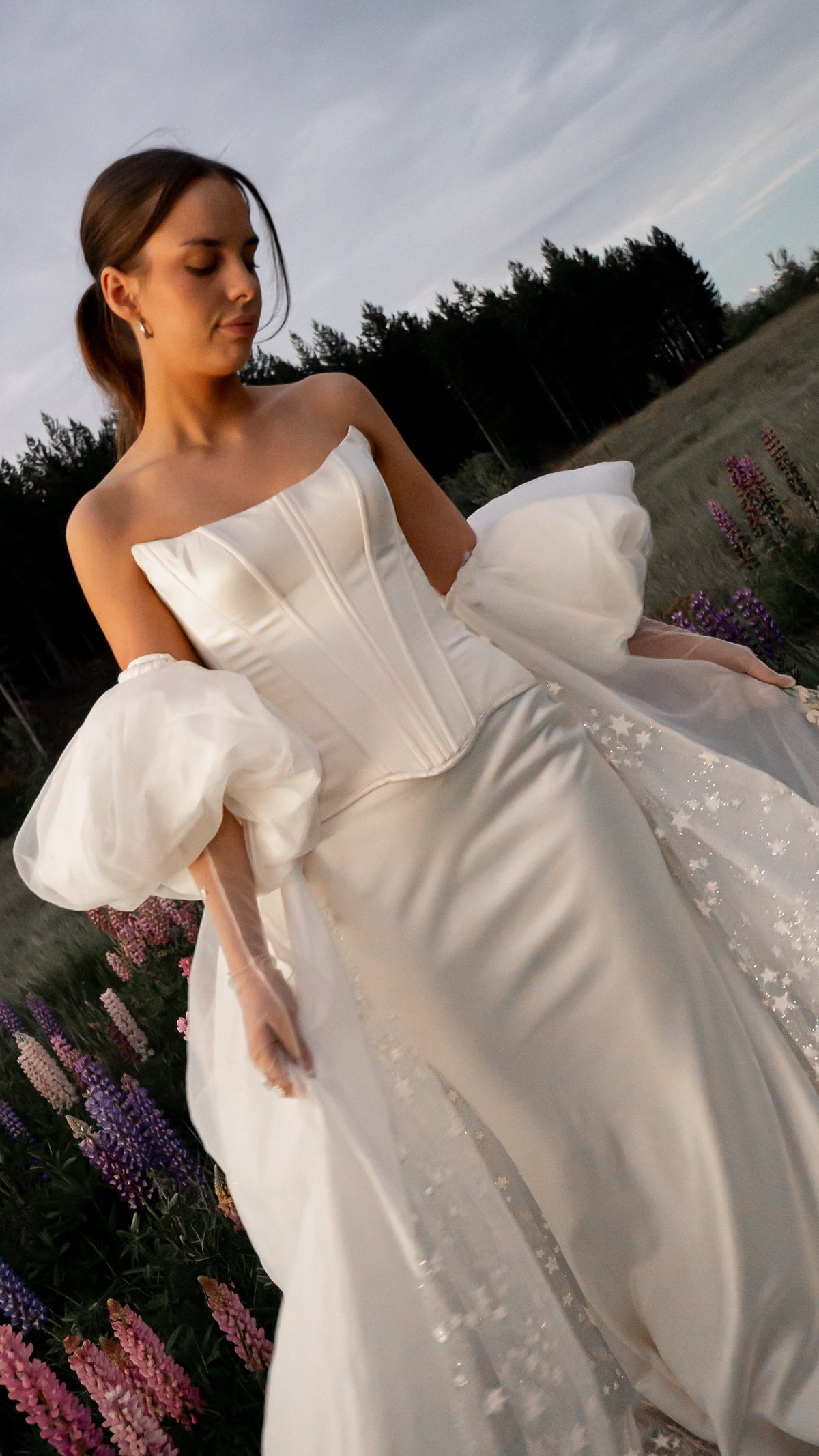 Bride walking through lupins in a satin bridal skirt with organza puff sleeves and a star lace overskirt, Solana Skirt