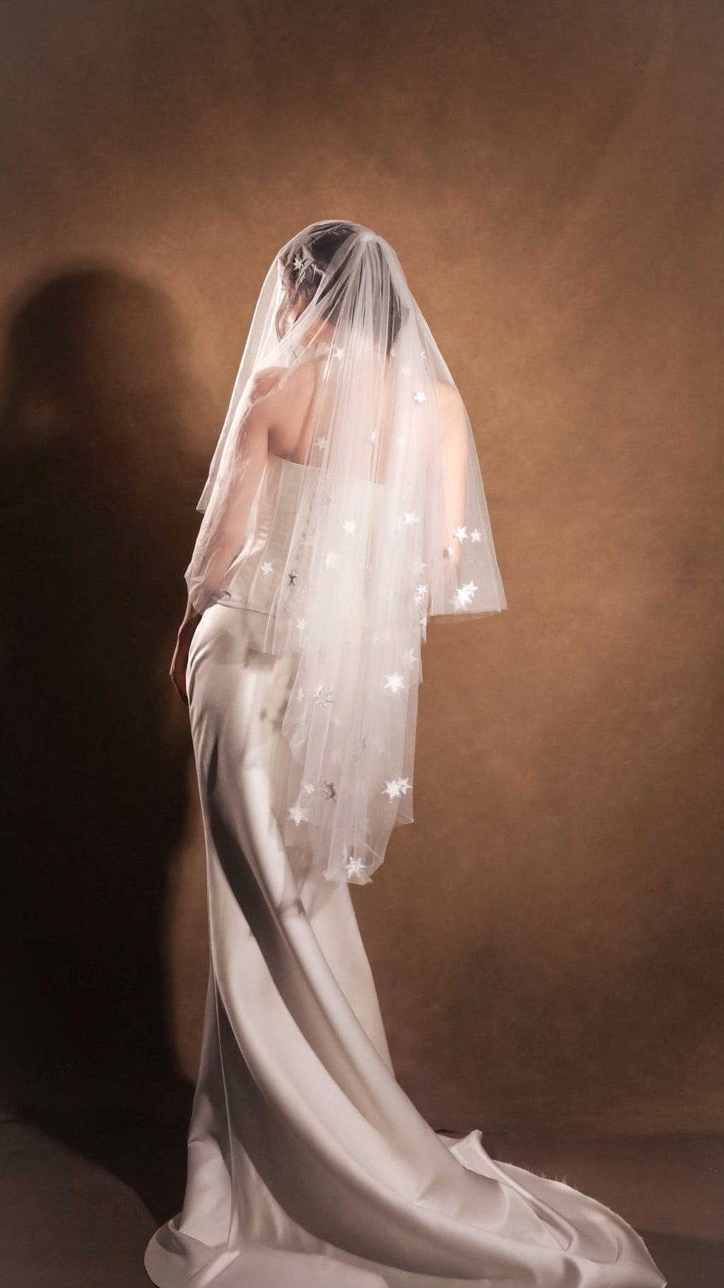 Three-quarter back view of a satin bridal skirt with a sweeping train, star-scattered veil over the face, Solana Skirt