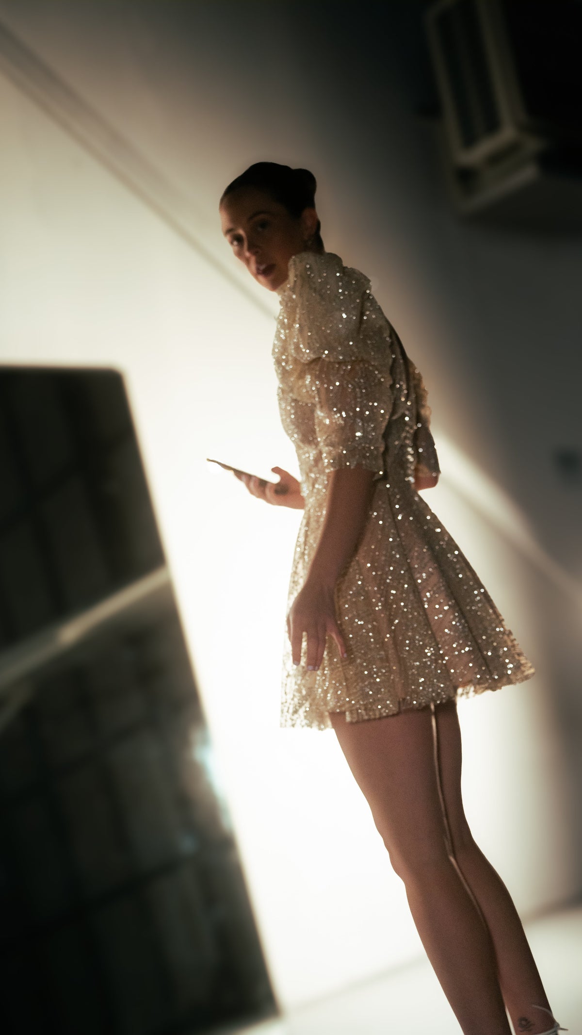 Side view of a champagne mini wedding dress with structured puff sleeves, model glancing back in a backlit studio, Soleil