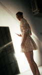 Side view of a champagne mini wedding dress with structured puff sleeves, model glancing back in a backlit studio, Soleil