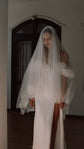 Raw-cut fingertip wedding veil worn over the face, fuller front in fine tulle, bride by arched doors in a slit gown, Spell Veil by Ephemeris