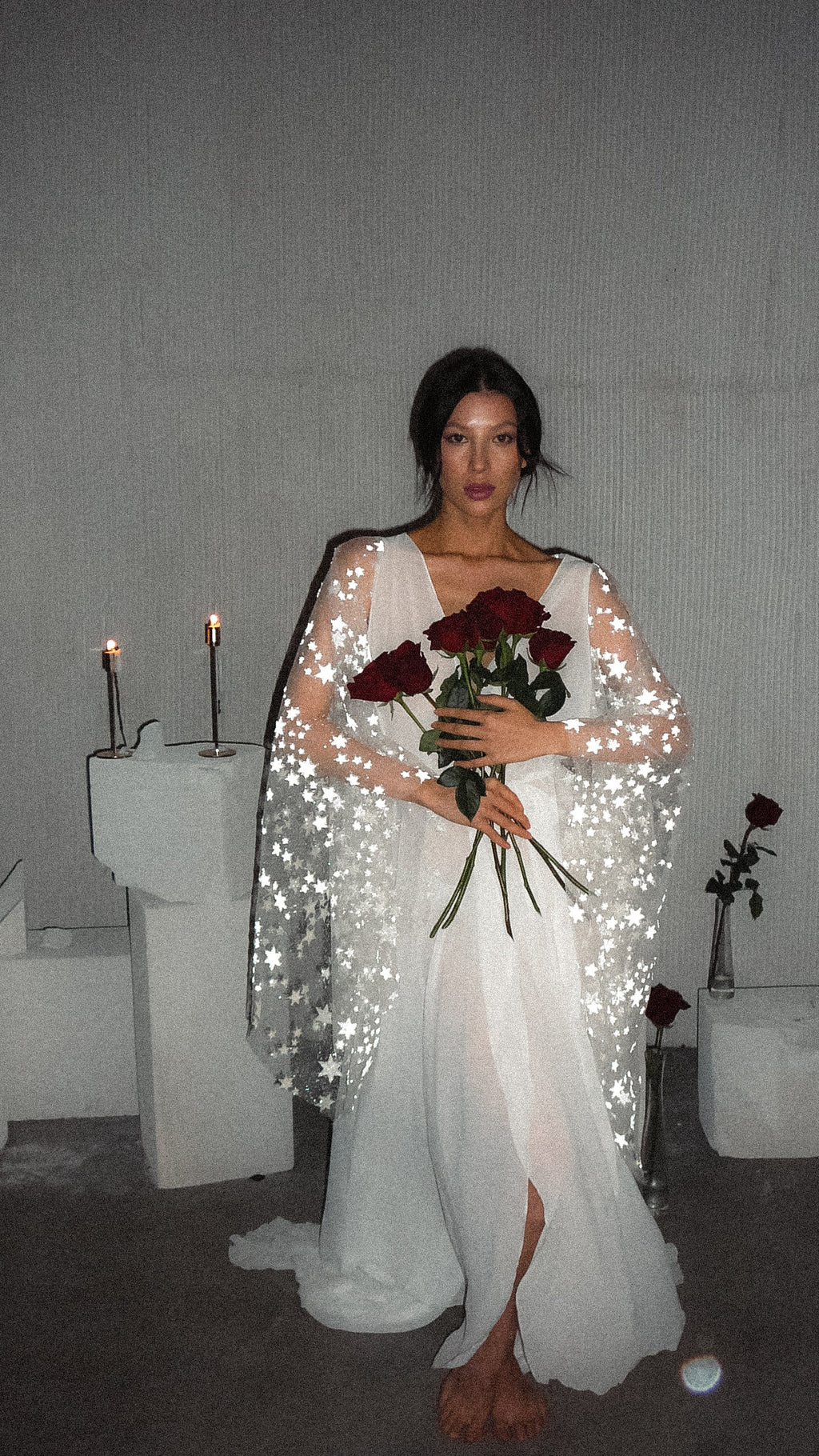 Celestial bridal robe in flowing chiffon with star lace bell sleeves, bride holding red roses by candlelit plinths, Stargazer Robe Ivory by Ephemeris