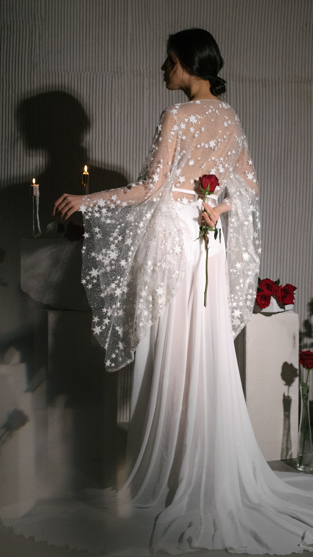 Back view of a getting-ready bridal robe with a sheer star lace back, bride holding a red rose behind her, Stargazer Robe Ivory