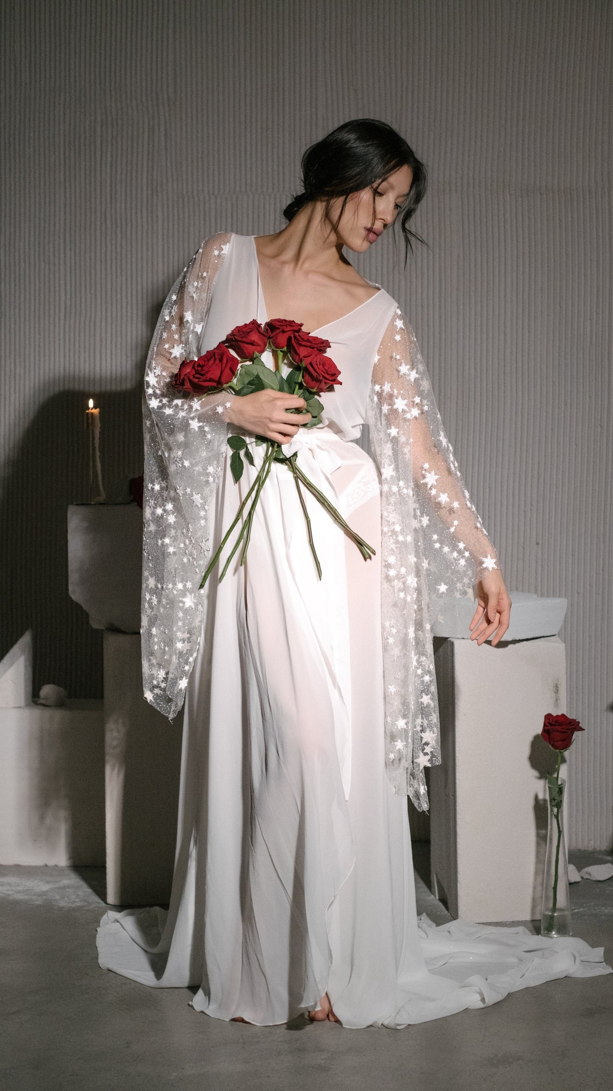 Front view of a chiffon bridal robe with wide star lace sleeves, bride looking down at a bunch of red roses, Stargazer Robe Ivory