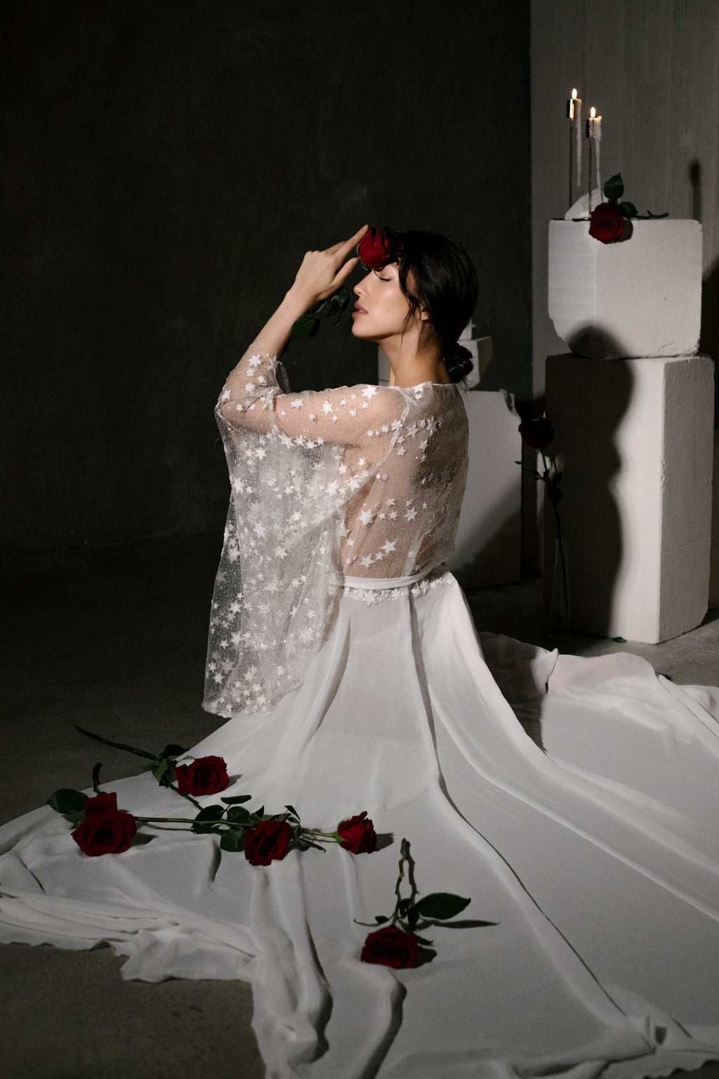 Bride kneeling with her chiffon bridal robe spread across the floor, star lace sleeves and scattered red roses, Stargazer Robe Ivory