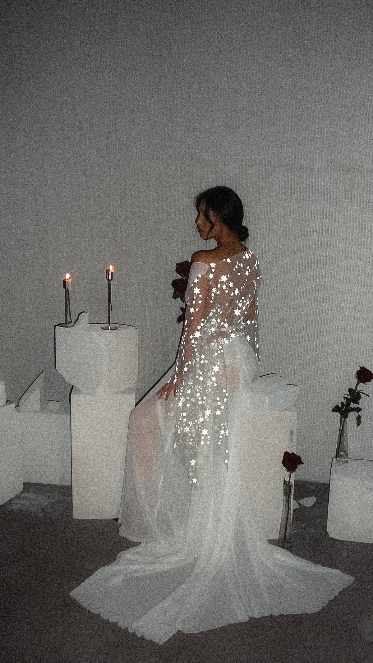 Bride sitting on a white plinth seen from behind, star lace bridal robe with chiffon train fanned on the floor, Stargazer Robe Ivory