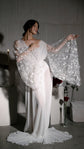 Bride hugging her shoulder in a bridal robe, one star lace sleeve opened like a wing over a pooled chiffon train, Stargazer Robe Ivory