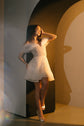 Short sparkle lace wedding dress with organza shoulders, model leaning on an arch with one hand in her hair, Starlight