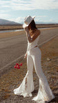 Back view of fitted bridal trousers with a long star lace flare, bride in a cowboy hat holding red roses by a country road, Sun Flares