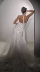 Back view of a fitted star wedding dress with a low open back and flared tulle train, model posed by a white arch, Supernova by Ephemeris