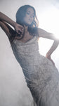 Close crop of a draped cowl neckline on a beaded star wedding dress, arms raised against bright backlight, Supernova