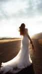 Bride walking down an open road at sunset in a low-back star wedding dress, tulle train and lupins in hand, elopement, Supernova