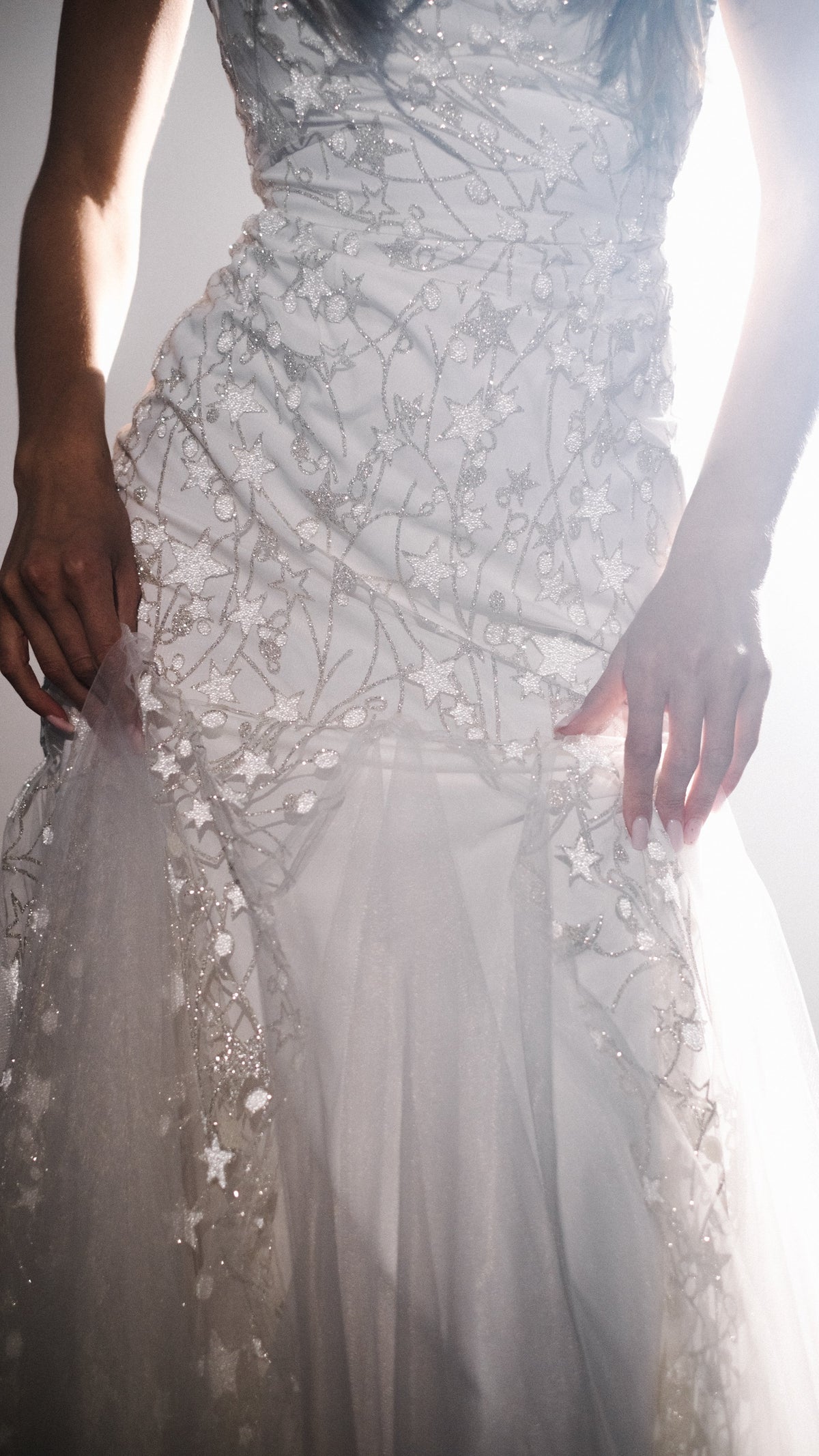 Close crop of the fitted bodice of a star wedding dress with reflective glass beads and tulle insets at the hips, Supernova