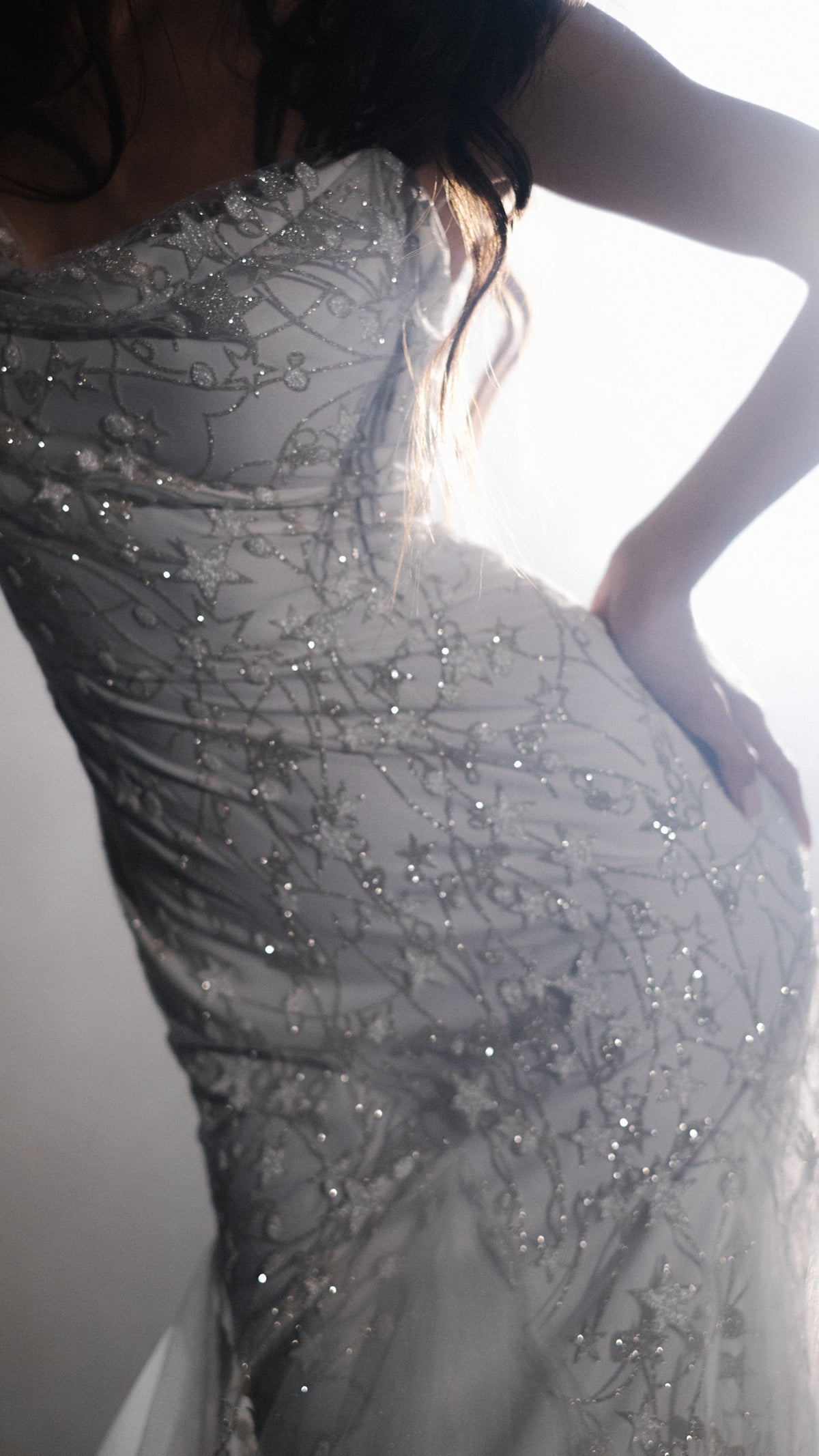 Detail of reflective glass beads and star motifs on the fitted bodice of a wedding dress, hand on hip, Supernova
