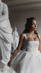 Satin corset mini wedding dress with a square neck, model glancing sideways among white statues, editorial, Swan