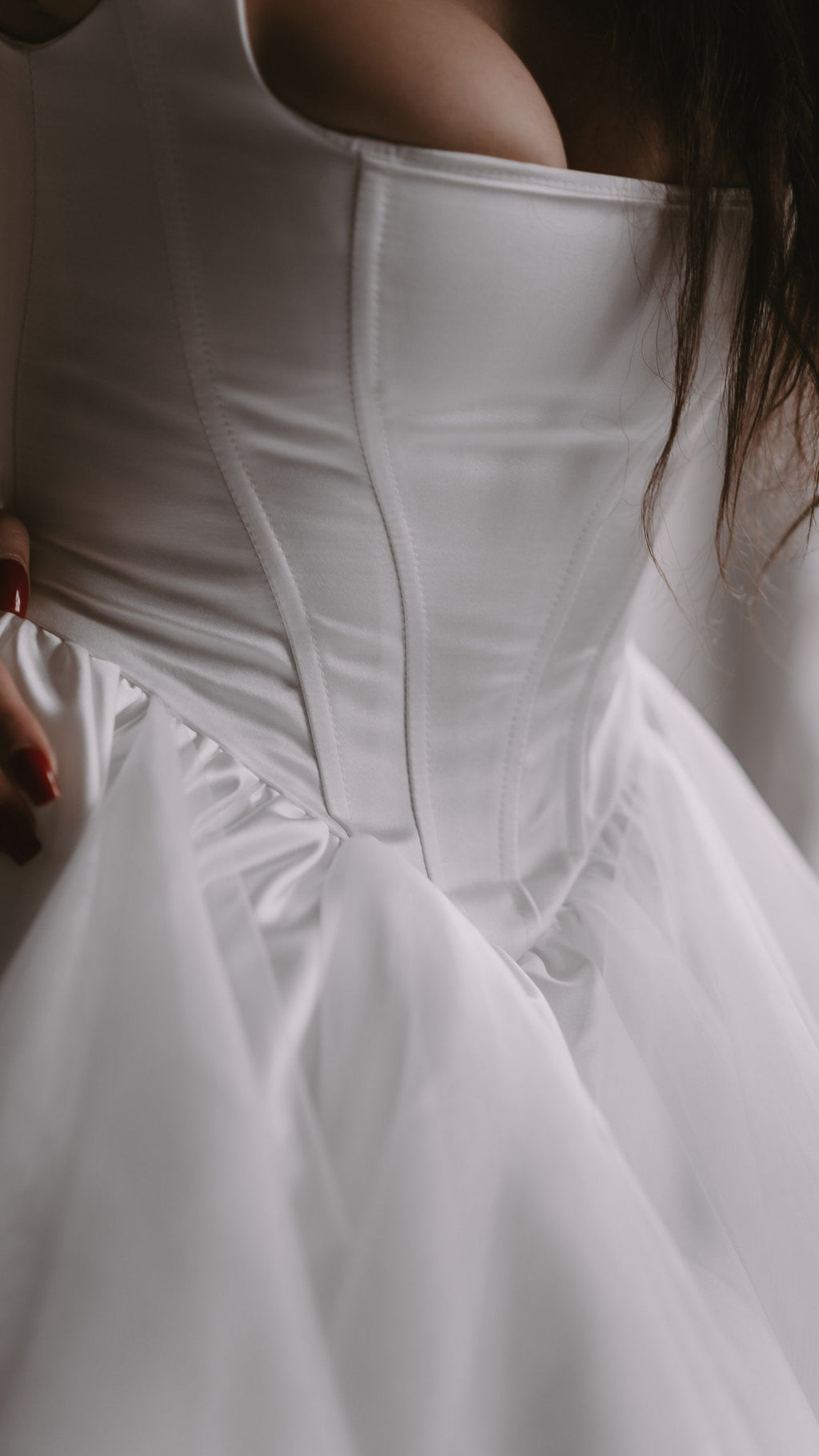 Close crop of a dropped basque corset on a satin wedding dress, boning lines meeting the tulle skirt, Swan