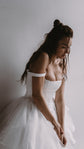 Satin corset wedding dress worn off the shoulder, model seated looking down over a full tulle skirt, Swan