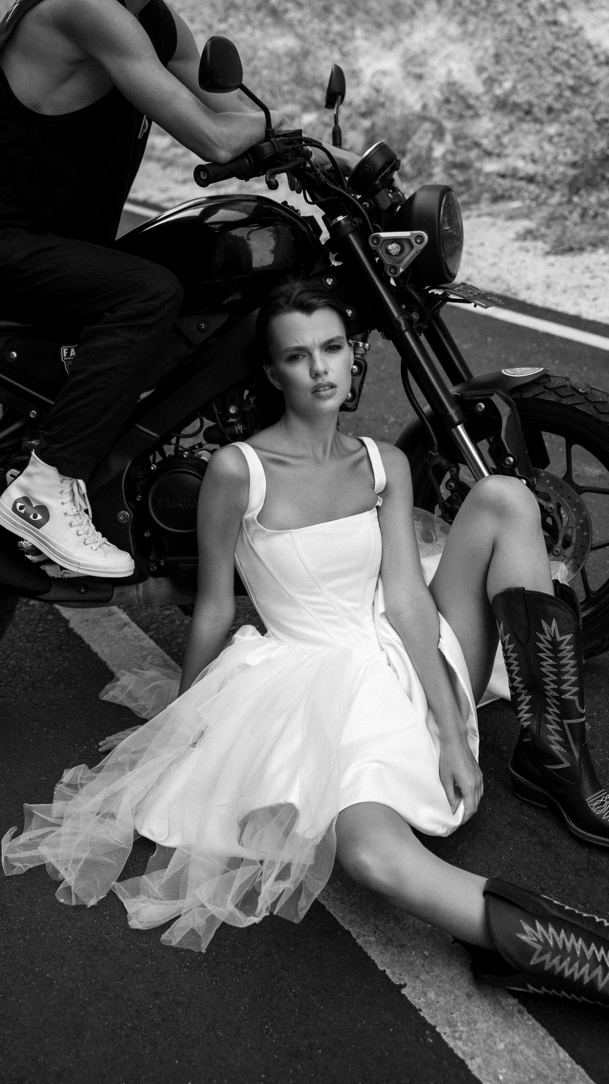 Bride sitting on the road against a motorbike in a corset mini wedding dress and cowboy boots, black and white, Swan