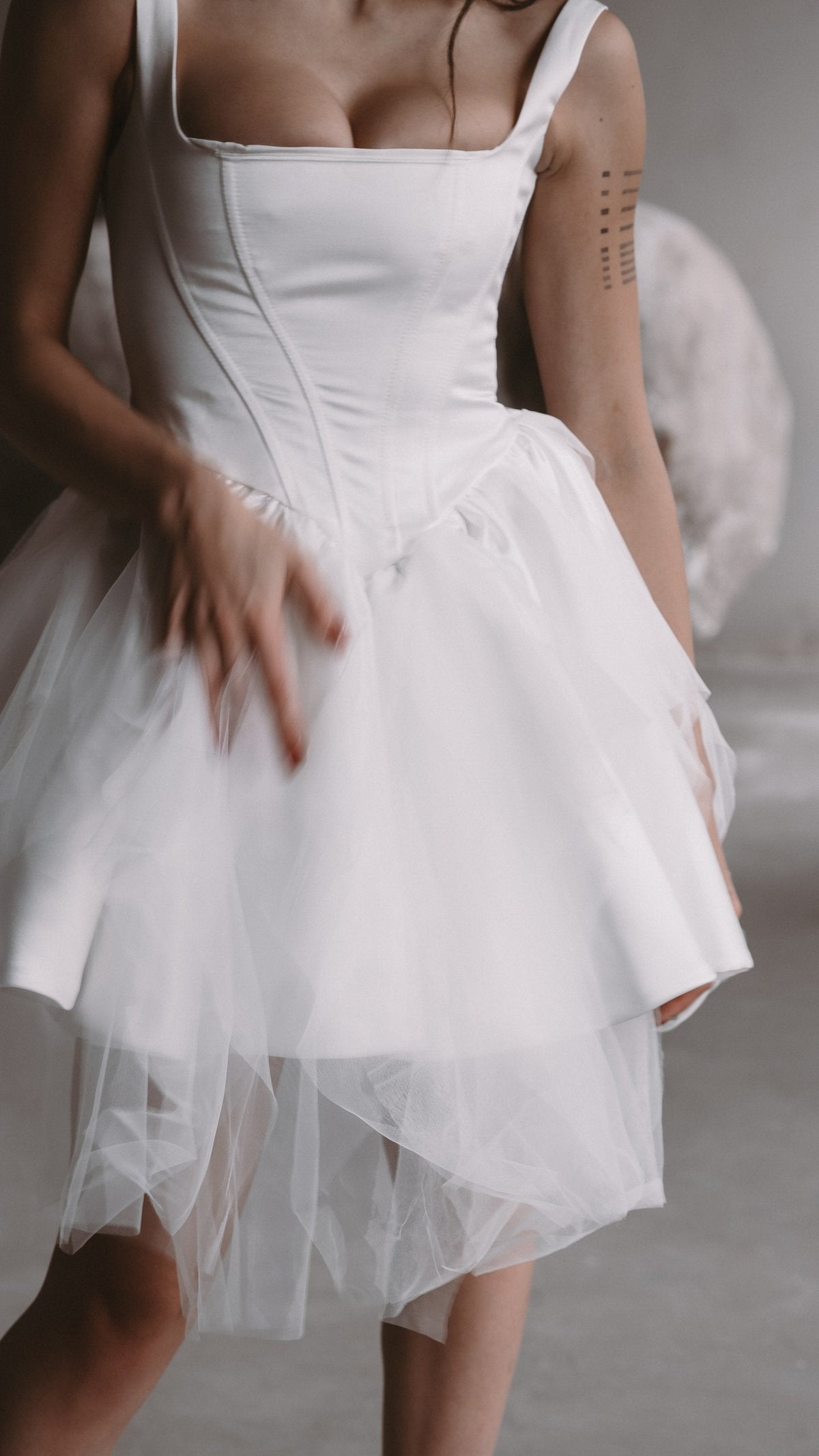 Torso crop of a square-neck satin corset wedding dress with a dropped basque waist and layered tulle skirt, Swan