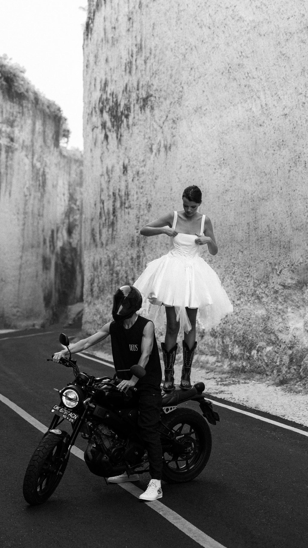 Bride standing on a motorbike seat in a short corset wedding dress, tulle mini skirt and boots, rider below, canyon road, Swan