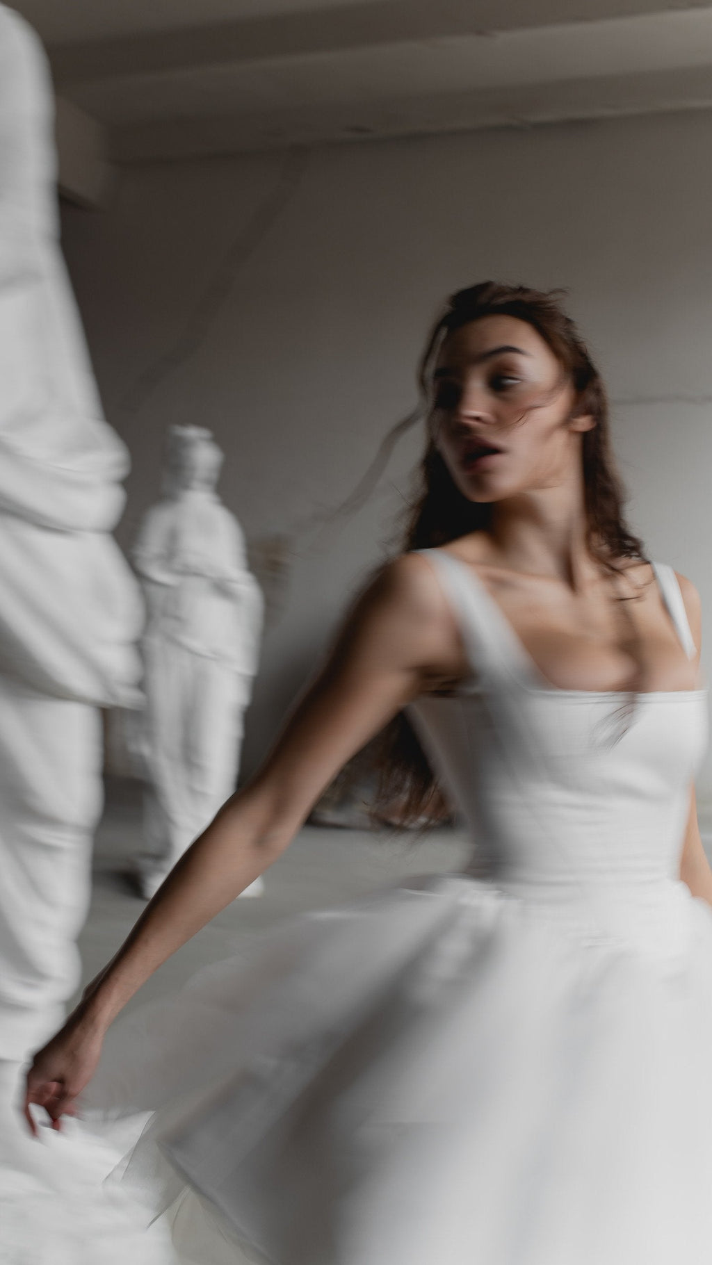 Motion blur of a satin corset wedding dress with wide straps and a tulle skirt, model turning past white statues, Swan
