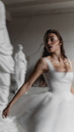 Motion blur of a satin corset wedding dress with wide straps and a tulle skirt, model turning past white statues, Swan