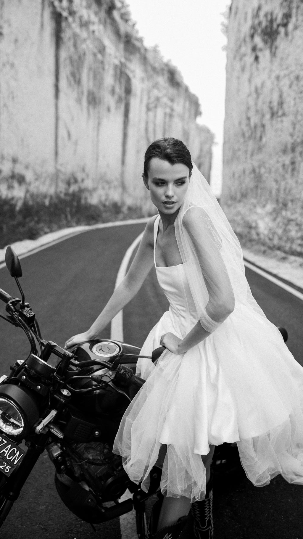 Bride in a short tulle veil leaning on a motorbike, square-neck corset mini wedding dress, black and white road shot, Swan