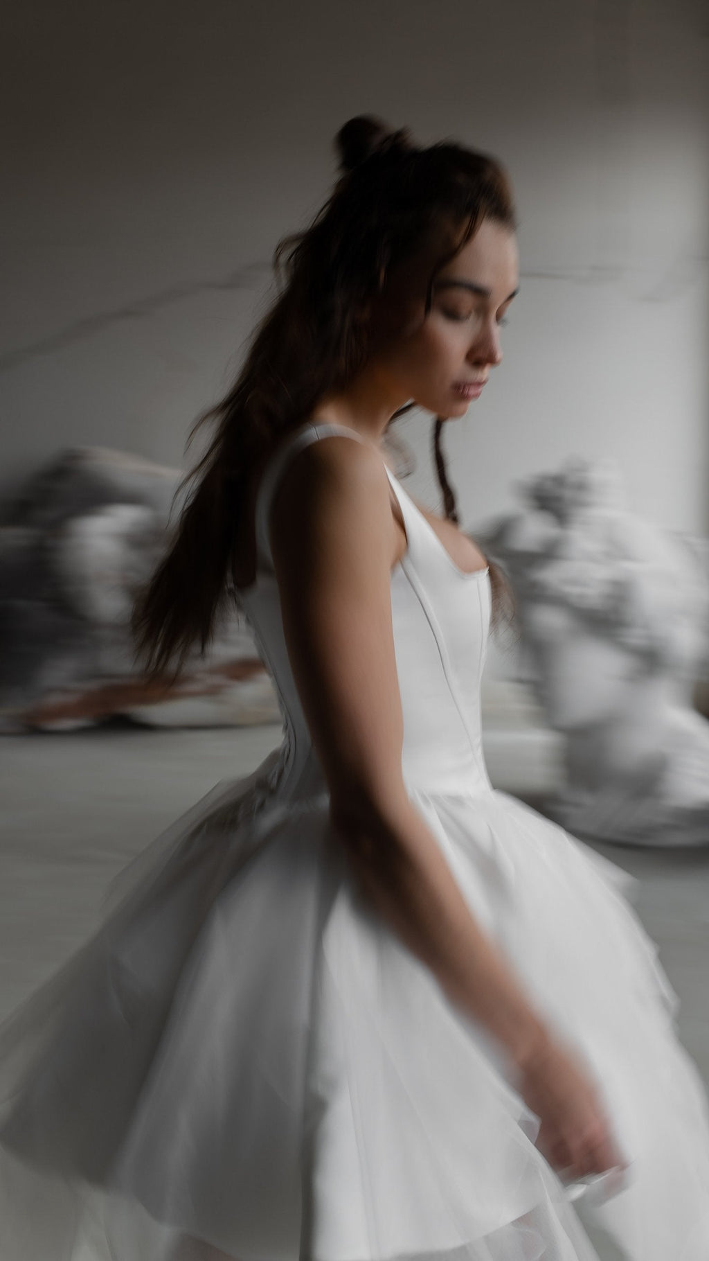 Side view of a satin corset mini wedding dress with a full tulle skirt, model looking down, soft blurred studio, Swan