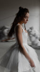 Side view of a satin corset mini wedding dress with a full tulle skirt, model looking down, soft blurred studio, Swan