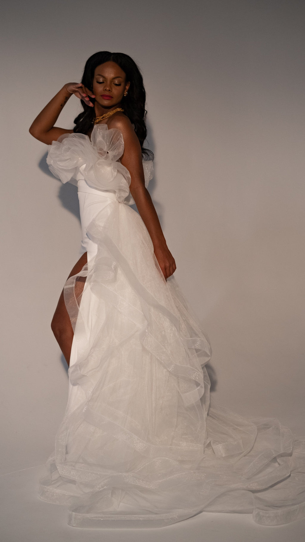 Model touching her hair in a fitted crepe sample wedding dress with a tiered tulle overskirt to the floor, Terra Sample