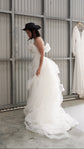 Bride in a black hat gathering the tulle overskirt of a crepe sample wedding dress, metal shed with a hanging gown, Terra Sample
