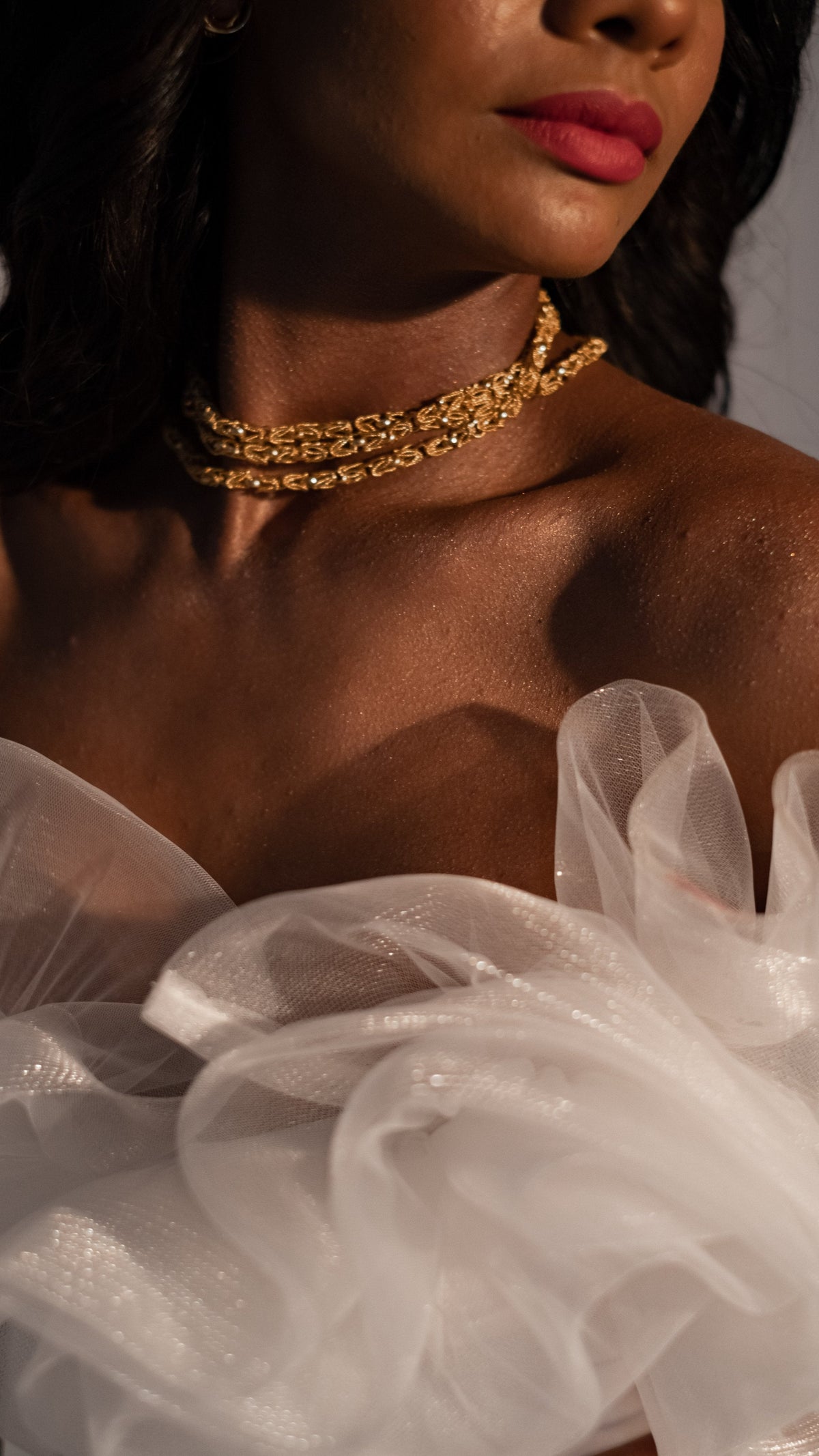 Detail of the ruffled tulle neckline of a sample wedding dress with a gold chain necklace, warm studio light, Terra Sample