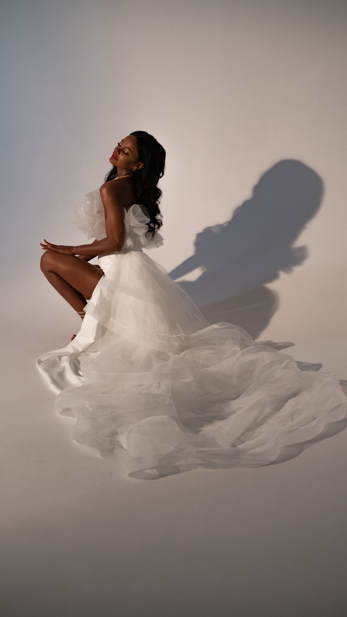 Model crouching in a sample wedding dress with the tulle overskirt spread in waves across the studio floor, Terra Sample