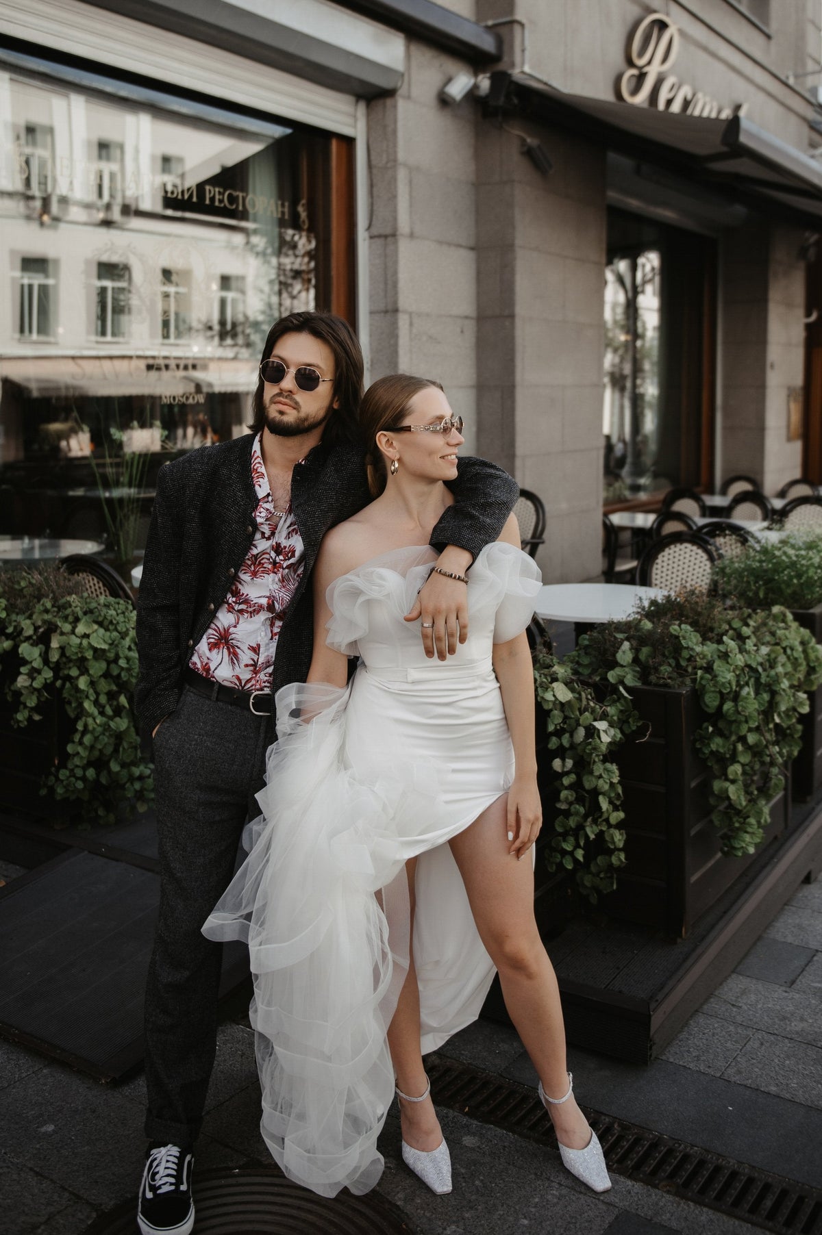 Couple outside a city cafe, bride in an off-shoulder wedding dress with a thigh-high slit and tulle overskirt, Terra