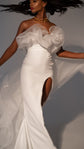 Fitted crepe wedding dress with a sculpted tulle ruffle neckline and slit, model turning with the overskirt lifted, Terra