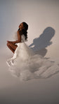 Model crouched mid-pose in an off-shoulder wedding dress with the tulle overskirt pooled around her, Terra