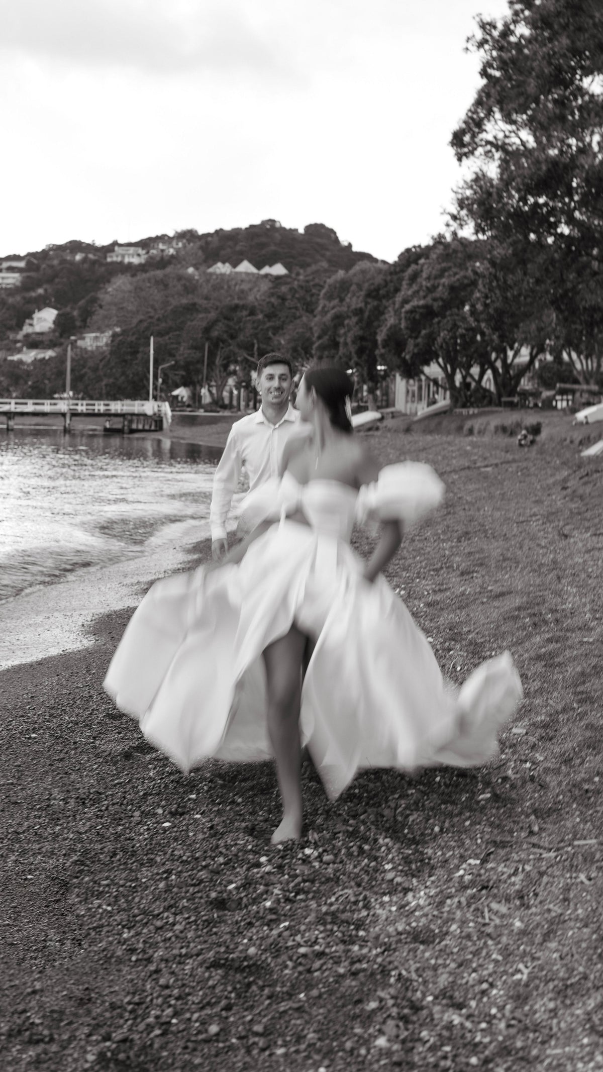 Glossy satin wedding dress with a bandeau bodice and puff sleeves, bride running barefoot on a pebble beach, The Dark Side of The Moon by Ephemeris