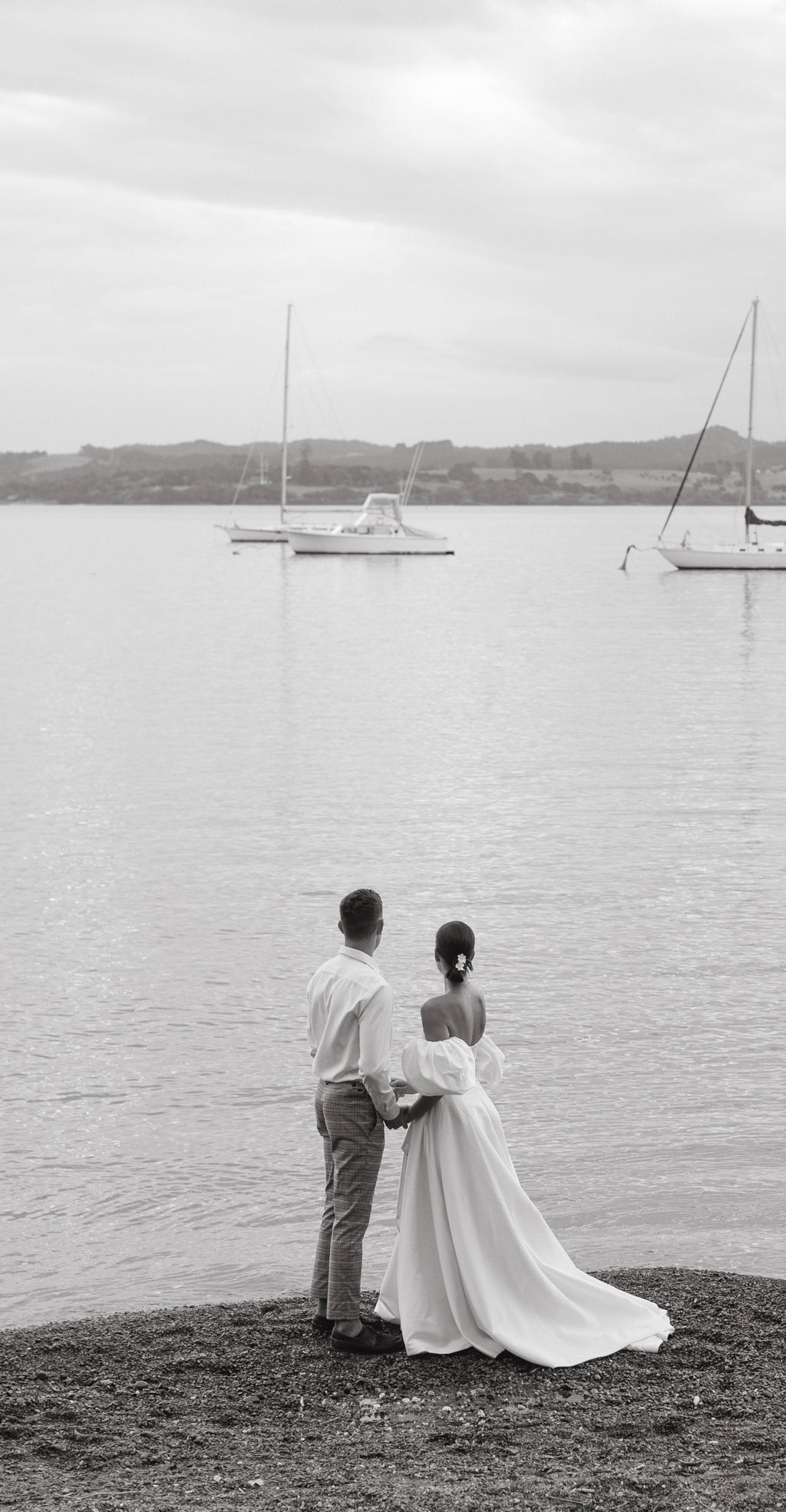 Couple on the shore looking at moored boats, bride in a strapless satin wedding dress with a long train, The Dark Side of The Moon