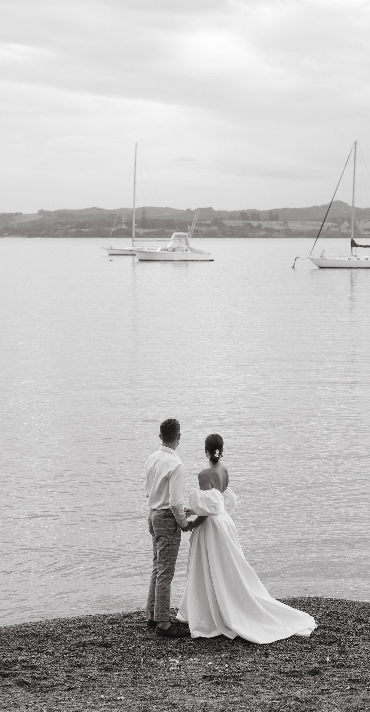 Couple on the shore looking at moored boats, bride in a strapless satin wedding dress with a long train, The Dark Side of The Moon