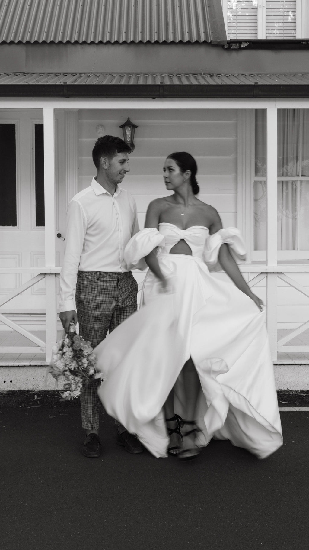 Bride lifting the skirt of a satin wedding dress with a bandeau bodice and puff sleeves beside the groom, The Dark Side of The Moon