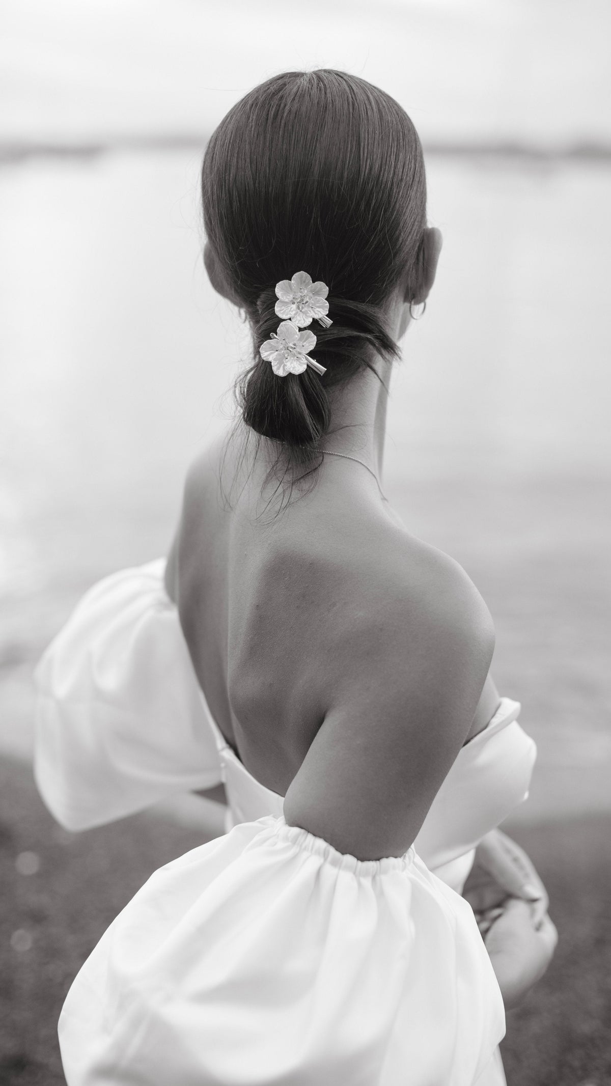 Close back view of a satin wedding dress with gathered puff sleeves, flower clips in a low bun, sea behind, The Dark Side of The Moon