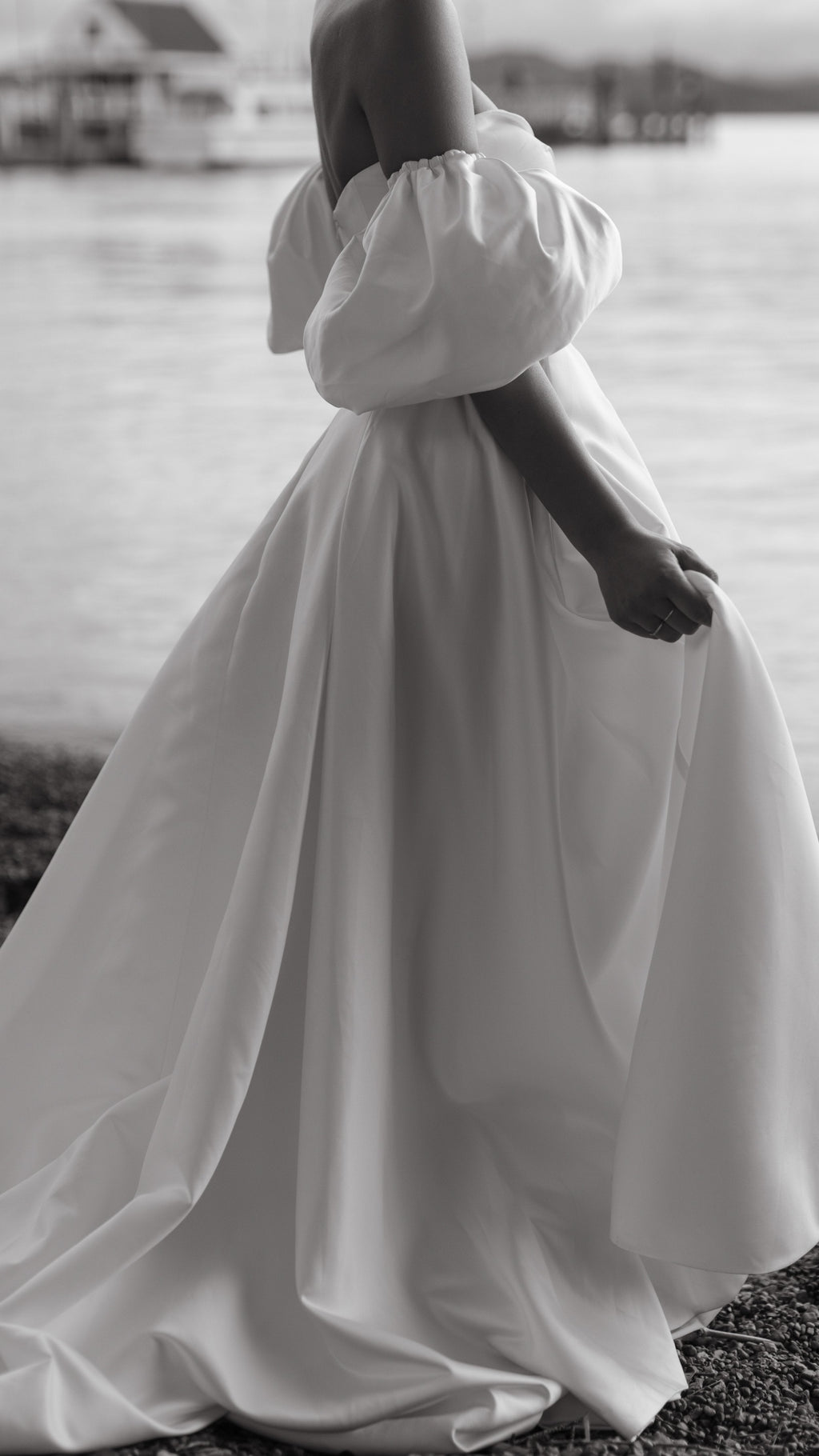 Side crop of a satin wedding dress with a full skirt and puff sleeve, bride holding the fabric by the water, The Dark Side of The Moon